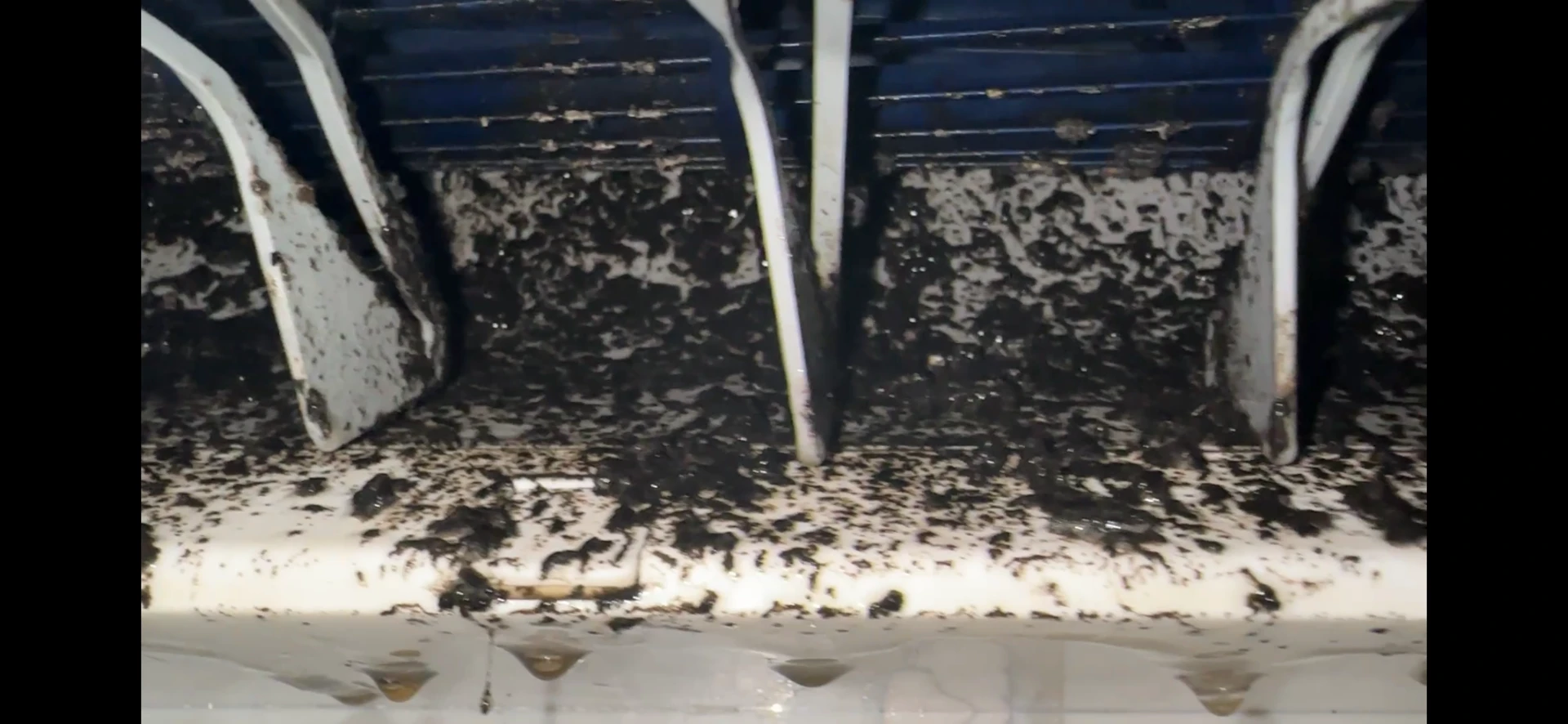 Heavy dust and grime buildup inside a wall-mounted heat pump blower and coil before cleaning